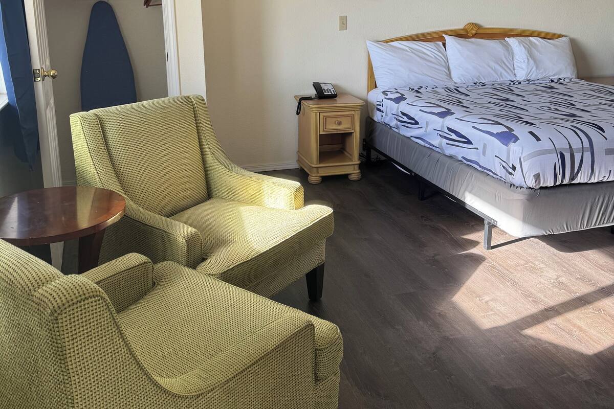 A hotel room with a bed, a chair, a small table, a lamp, and a painting on the wall.