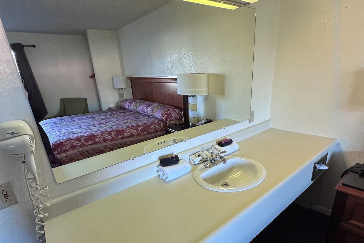 A hotel room with a bed, a large mirror, a sink, and a telephone.