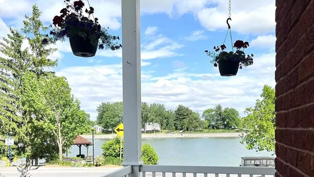 A wooden deck with hanging flower pots, a gazebo, and a view of a lake.