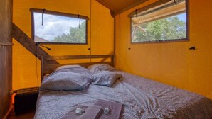 Et soveværelse med en træseng, to vinduer med gardiner og en trappe.