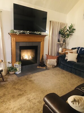 A living room with a fireplace, a television mounted above it, a dark blue sofa, and a potted plant.