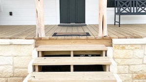 A wooden porch with a dark door, two wall-mounted lanterns, and a welcome sign. - The Ranch@Fredericksburg - Magnolia Cottage - 1BD/1BA (Fredericksburg)