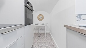 A compact kitchen with white cabinetry, a patterned floor, and a round decorative mirror on the wall.