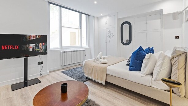 A modern living room with a TV, a round coffee table, a sofa with blue and white cushions, and a large window.
