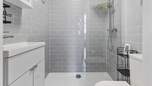 Ein modernes Badezimmer mit grauen Fliesen, einer Dusche, einer Toilette und einem Waschbecken.