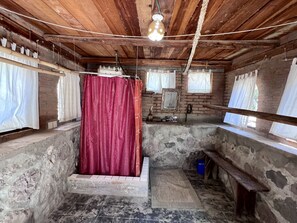 Un baño rústico con techo de madera, cortina de ducha roja y pared de piedra.
