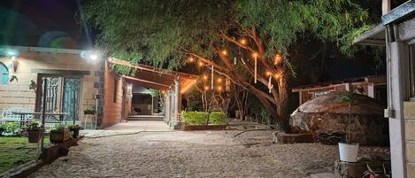 Un cortile con un vialetto in pietra, una pergola con luci a stringa e un forno rustico in pietra.