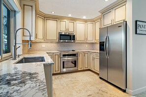 A kitchen with beige cabinetry, a stainless steel refrigerator, a microwave, and an oven.