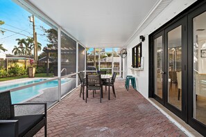 Eine überdachte Terrasse mit Pool, Sitzgelegenheiten im Freien und einer Glasschiebetür zu einer Terrassenfläche.