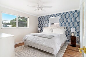 A bedroom with a bed, a ceiling fan, a window, and a patterned wall.