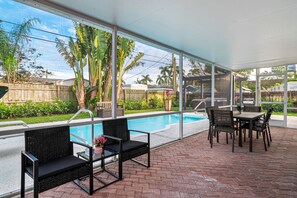 A covered patio area with a pool, outdoor furniture, and a view of the backyard.