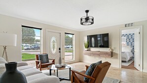 Een ruime woonkamer met een grote televisie, comfortabele zithoek en uitzicht op buiten.