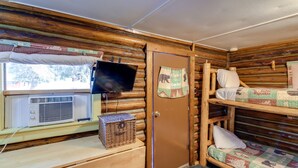 Une cabine équipée de lits superposés, d’un téléviseur, d’une fenêtre avec des rideaux et d’un bureau en bois avec un panier.