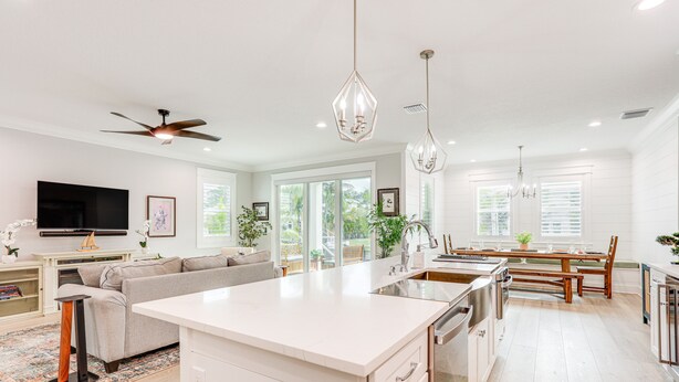 A modern kitchen with a central island, white cabinetry, and stainless steel appliances. There is a dining area with a wooden table and chairs, and a large window providing natural light. - Private Pool: Waterfront Stuart Townhome! (Stuart)