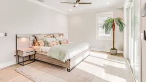 A bedroom with a bed, bedside table, nightstand, ceiling fan, large window, and a potted plant. - Private Pool: Waterfront Stuart Townhome! (Stuart)