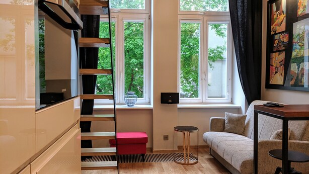 A modern living room with a staircase, a sofa, a small table, and a window with a view of greenery.