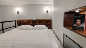 A neatly made bed with white linens, a wooden headboard, and two wall-mounted lights.
