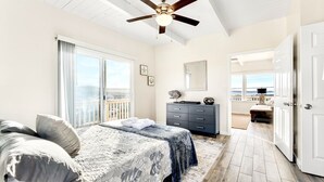 A bedroom with a bed, a ceiling fan, a dresser, and a view of the ocean.