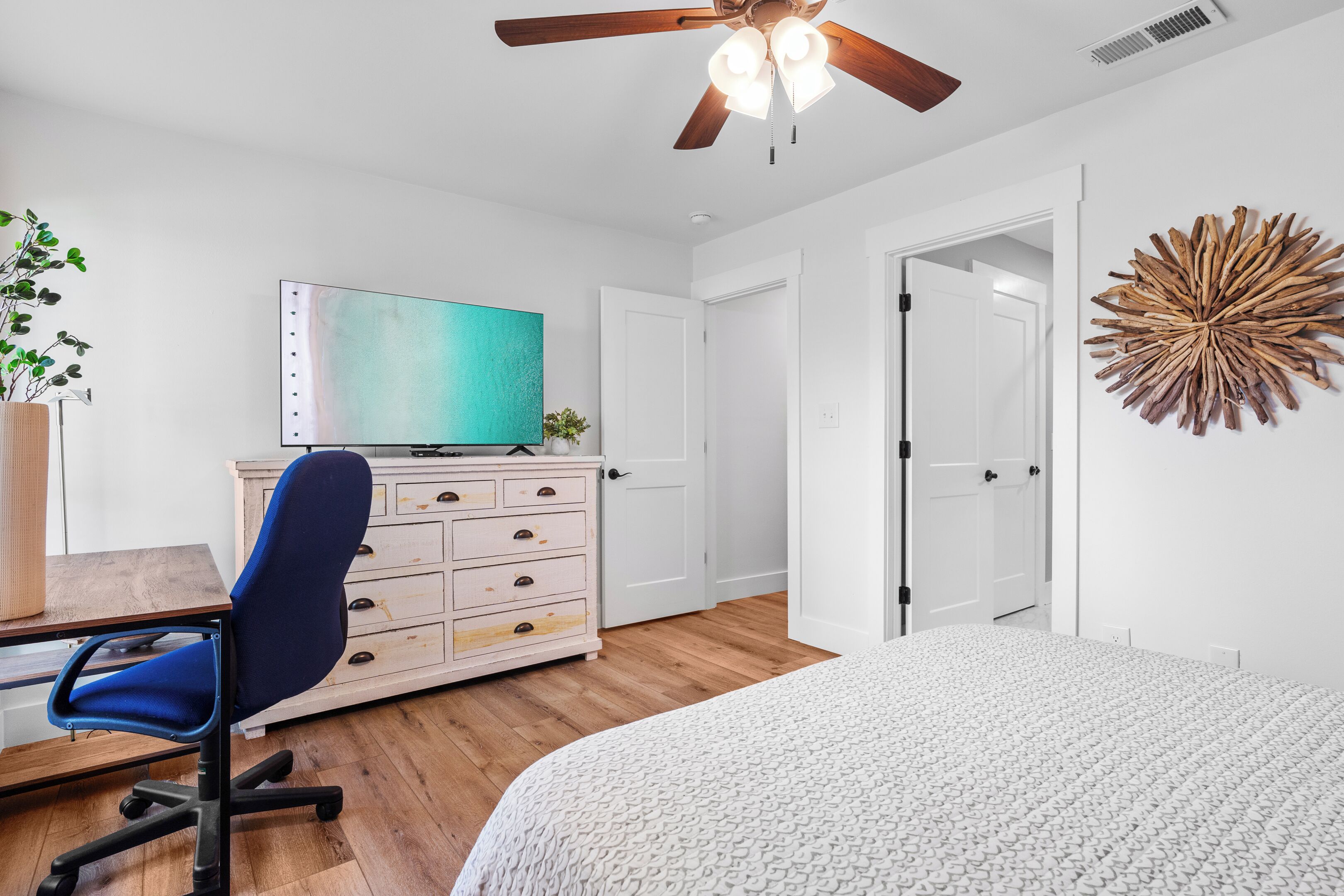A bedroom with a bed, a desk with a chair, a television, and a ceiling fan.