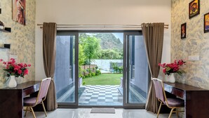 Une pièce avec un bureau et une chaise, un sol à carreaux et une vue sur un jardin et des collines.