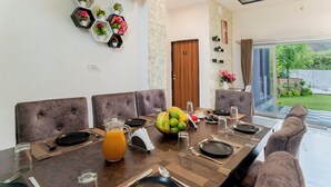 Un coin repas avec une longue table dressée pour quatre personnes, comprenant un panier de fruits, des assiettes, des couverts et des verres.