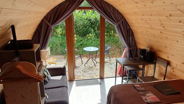 A cozy, wooden interior with a bed, a table, and a seating area. - Priory Glamping Pods (Killarney)