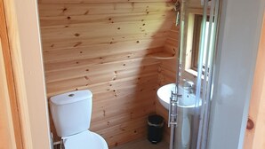 A wooden-paneled bathroom with a toilet, sink, and glass shower enclosure. - Priory Glamping Pods (Killarney)