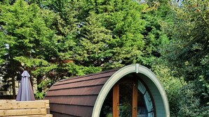 A cozy, semi-open structure with a curved roof, surrounded by lush greenery and a gravel path leading to it. - Priory Glamping Pods (Killarney)
