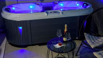 Un jacuzzi con panel de control, dos copas de vino y una botella de champán sobre una mesita.