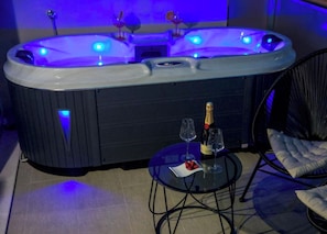 A hot tub with a control panel, two wine glasses, and a bottle of champagne on a small table. - Priory Glamping Pods (Killarney)