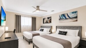 A hotel room with two beds, a desk, a TV, and artwork on the walls.