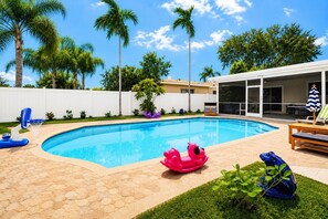 Une piscine dotée d’une terrasse carrelée en forme d’hexagone, entourée de palmiers et délimitée par une clôture blanche.