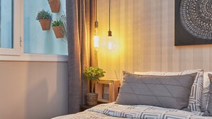 A bedroom with a bed, pillows, a bedside table with a lamp, and potted plants.