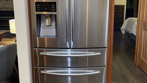 Een koelkast van roestvrij staal met een waterdispenser, onder houten keukenkastjes, in een moderne keuken met een houten vloer.