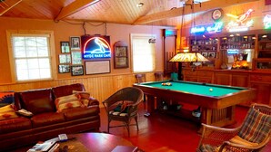 A cozy indoor setting with a pool table, leather sofas, and a bar area.