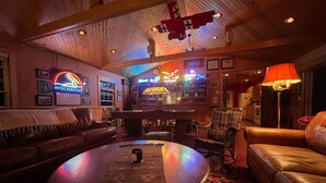 A cozy lounge area with leather sofas, a pool table, and a bar with neon signs.