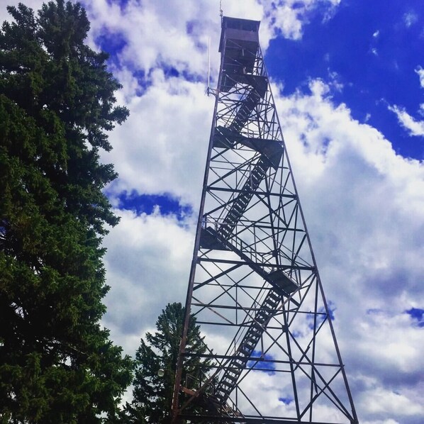 Ein hoher Metallturm mit einer Treppe, umgeben von Bäumen und einem teilweise bewölkten Himmel.