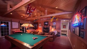 A pool table in a room with wooden walls and ceiling, a leather sofa, and a neon sign.