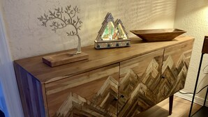 Um armário de madeira com padrão em espinha de peixe, uma pequena escultura de árvore e um objeto decorativo em cima.