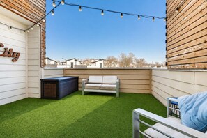 A rooftop patio with artificial grass, a white sofa, a small table, and string lights.