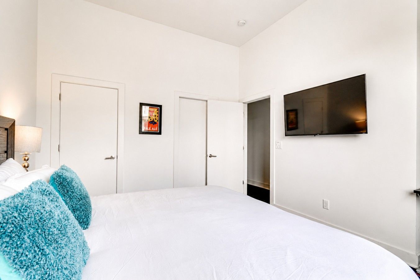 Ein Hotelzimmer mit einem Bett, einem an der Wand befestigten Fernseher und einer Tür mit einem gerahmten Bild.