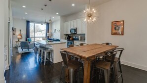 A modern kitchen with white cabinets, a wooden dining table, and bar stools. - King-bed townhome near The Gulch | 2-Car Garage (Nashville)