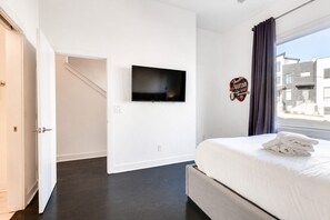A hotel room with a bed, a flat-screen TV mounted on the wall, a window with curtains, and a sign on the wall.