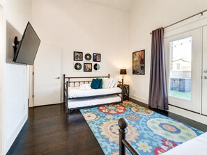 A bedroom with a bed, a TV mounted on the wall, a patterned rug, and a door leading to a balcony. - King-bed townhome near The Gulch | 2-Car Garage (Nashville)