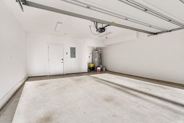 A spacious, empty room with a large white door, a ceiling-mounted projector, and a water heater in the background.