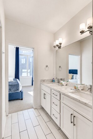 Un baño moderno con un espejo grande, muebles blancos y encimera de mármol.