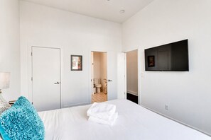 A hotel room with a bed, a TV mounted on the wall, and a bathroom visible through an open door.