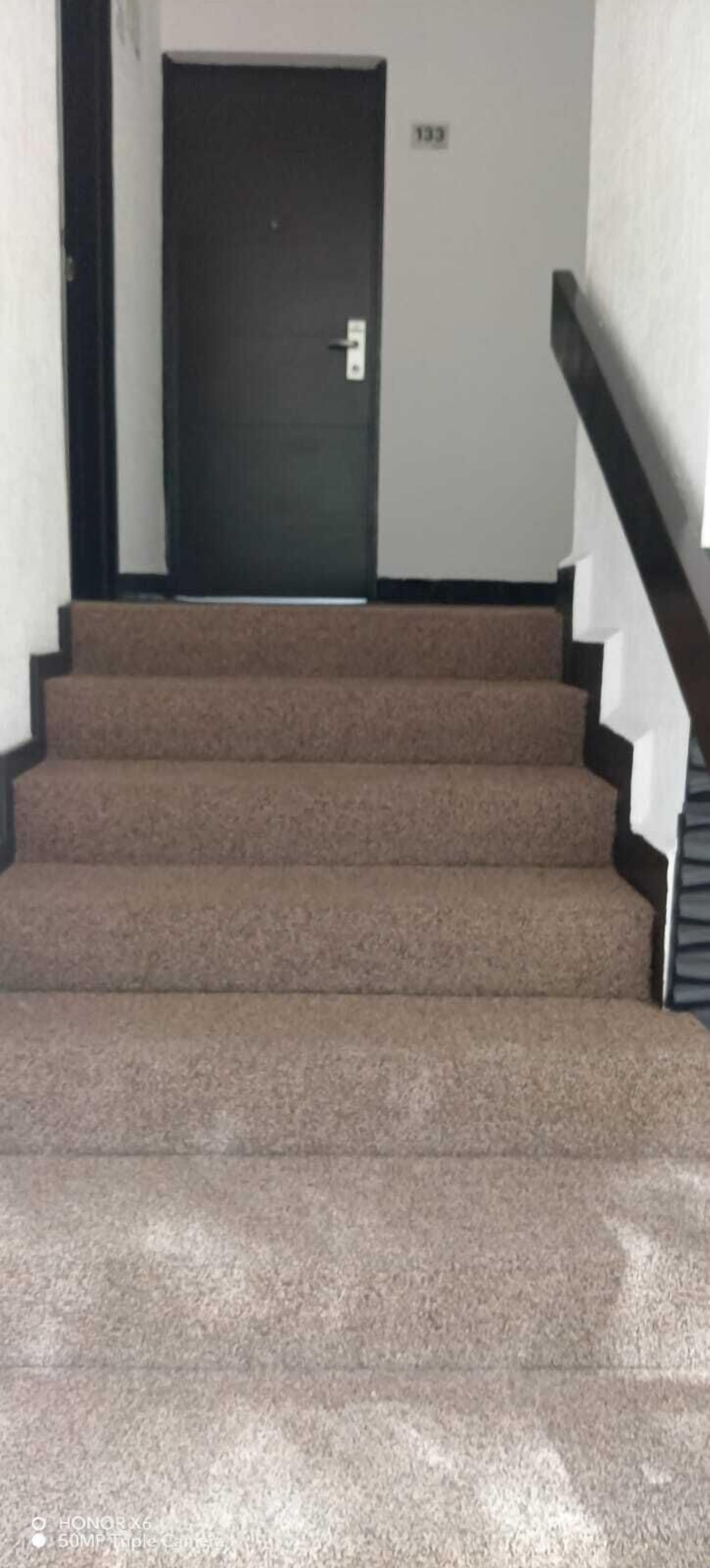 Una escalera alfombrada con una puerta oscura al final.