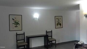 Een hotelkamer met een bed, een bureau, twee stoelen en twee ingelijste botanische prints aan de muur.