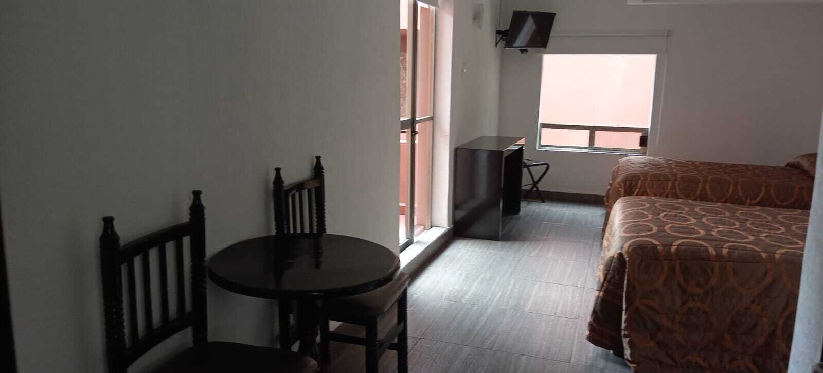 Una habitación de hotel con cama, una mesita, una silla, un televisor y una ventana.